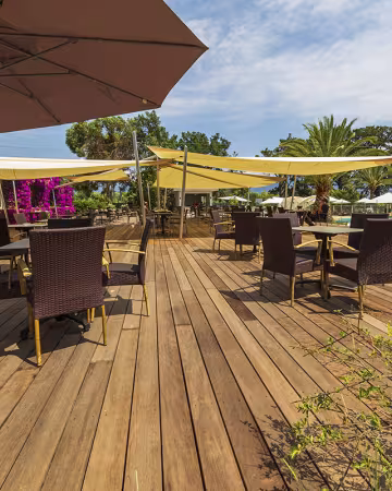 Terrasse en bois du bar, avec tables, parasols et bougainvilliers