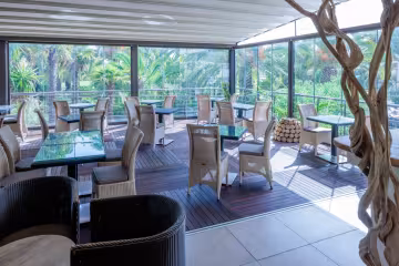 Véranda du restaurant, tables et fauteuils en osier face aux palmiers